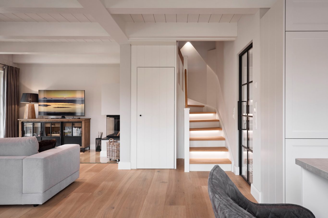 Treppenaufgang Helles Wohnzimmer mit Sofa, Fernseher und Treppe im Hintergrund. Minimalistischer Stil.