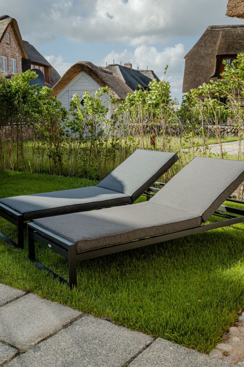 Komfortliegen Zwei Liegen auf einer grünen Rasenfläche vor einem modernen Haus.