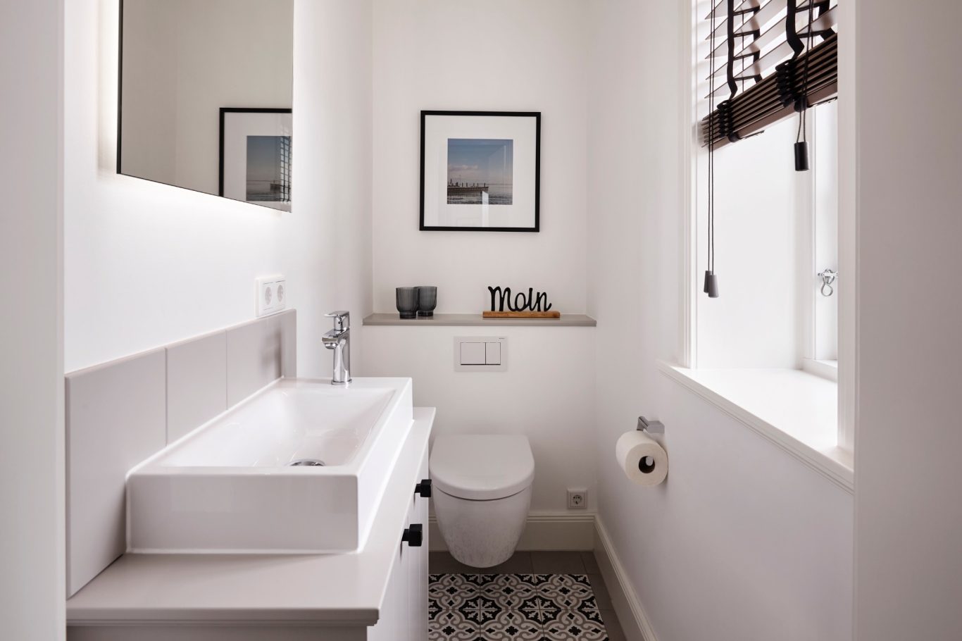 Gäste-WC Heller Badezimmer mit Waschbecken, WC, kunstvollem Bild und dekorativen Accessoires.