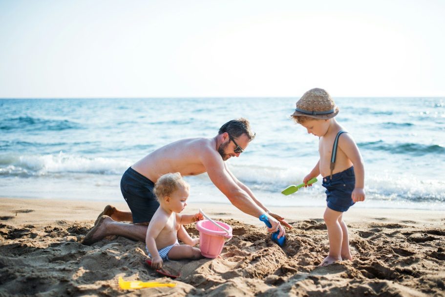 Strand auf Föhr Vater spielt mit zwei kleinen Kindern im Sand am Strand, während das Wasser plätschert.