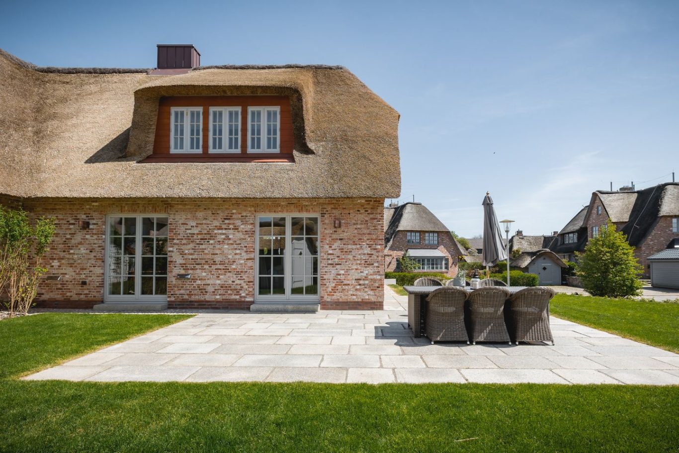 West-Terrasse Haus mit Reetdach, Terrasse und Gartenmöbeln in einer sonnigen Umgebung.