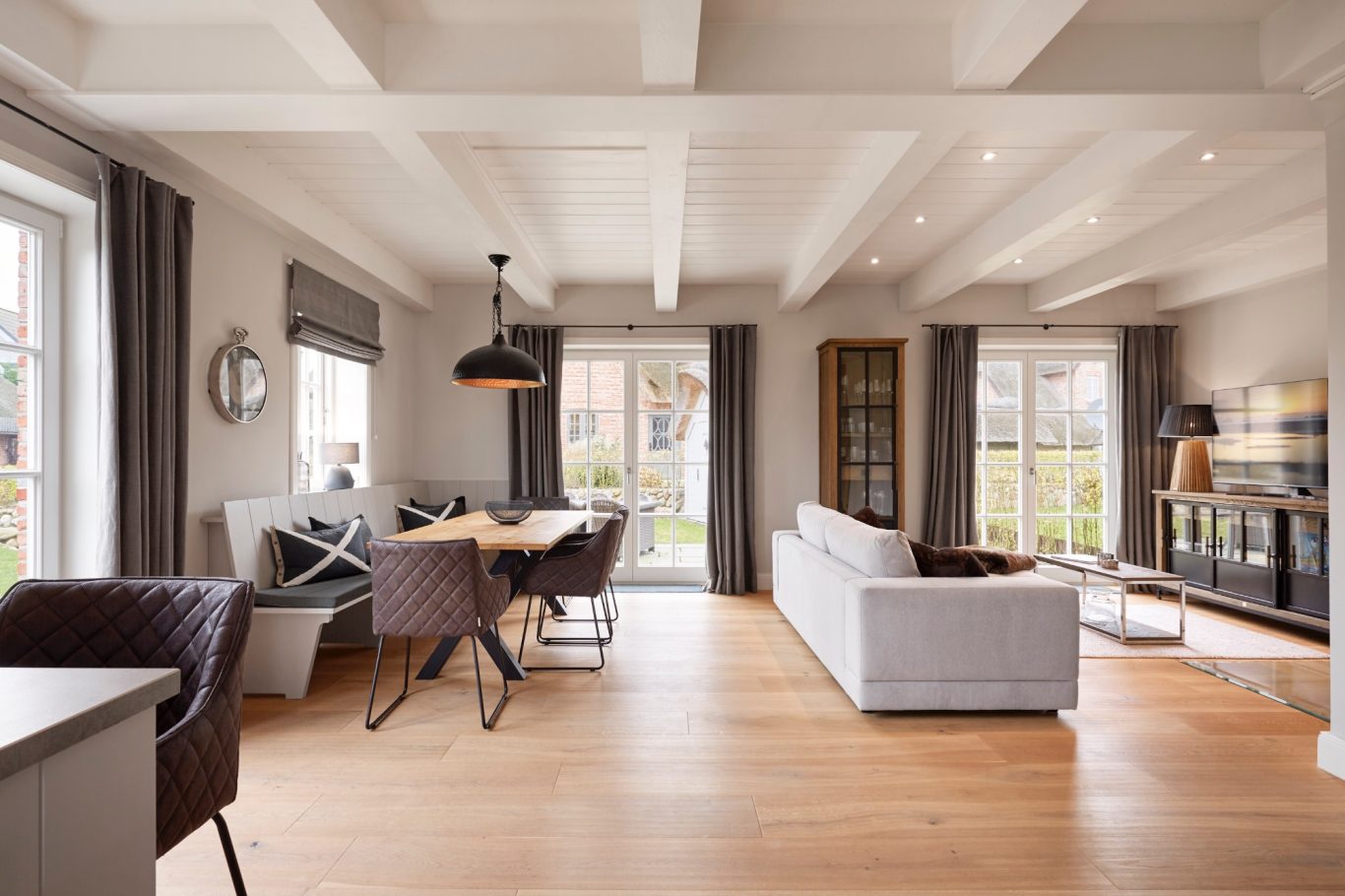 Wohn-/ Essbereich Helles Wohnzimmer mit Holzboden, großen Fenstern und moderner Einrichtung.