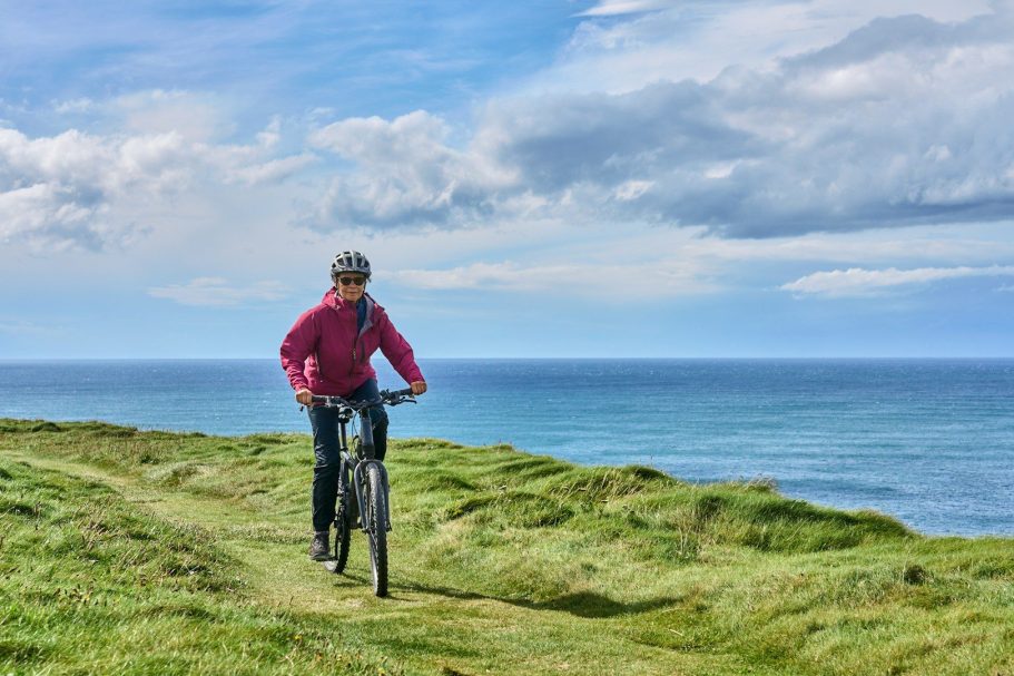 Radfahren an der Küste von Föhr. Radfahrer fährt auf einem Weg entlang der Küste mit Meerblick und bewölktem Himmel.