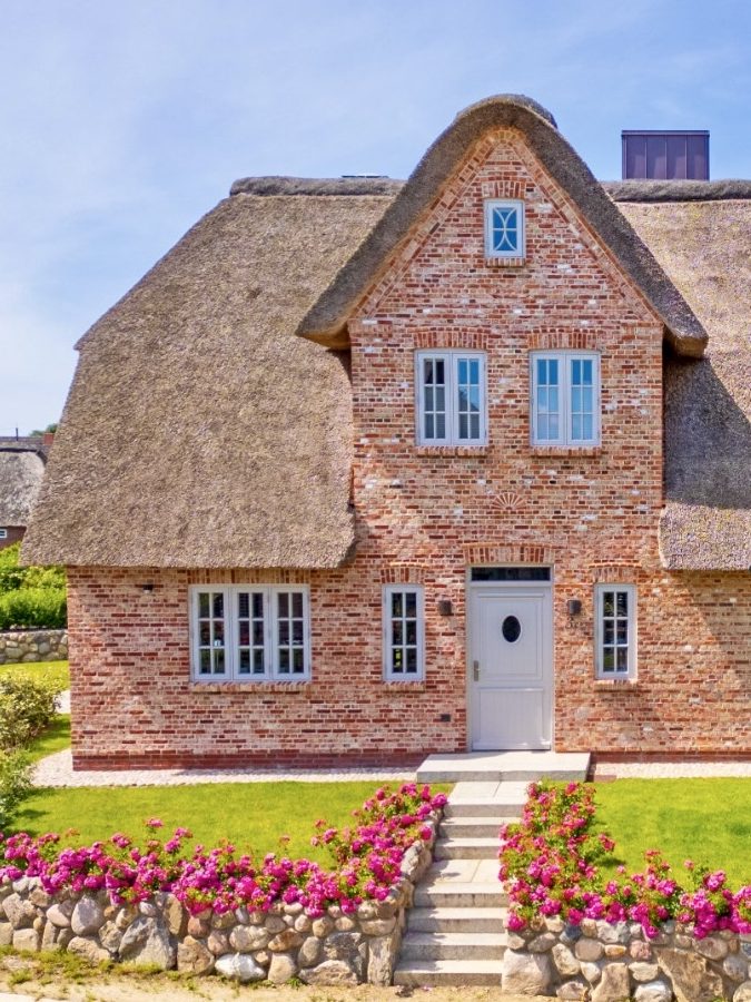 Front des Reethauses Nordgold Traditionelles, Ferienhaus mit Reetdach und bunten Blumen im Vorgarten.