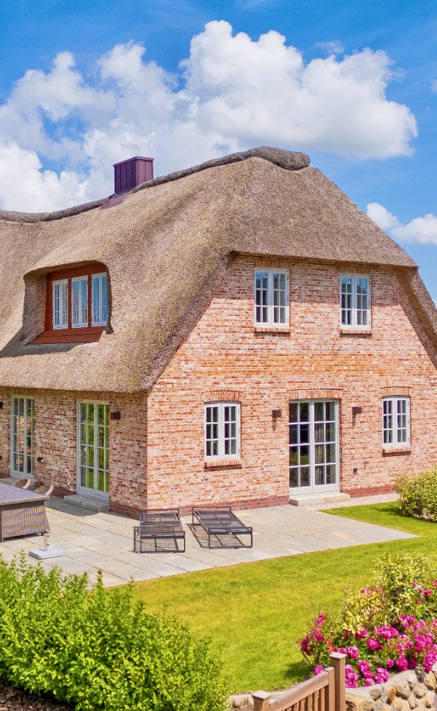 Garten Reethaus Nordgold Ferienhaus mit Reetdach, Garten und Terrasse unter blauem Himmel.